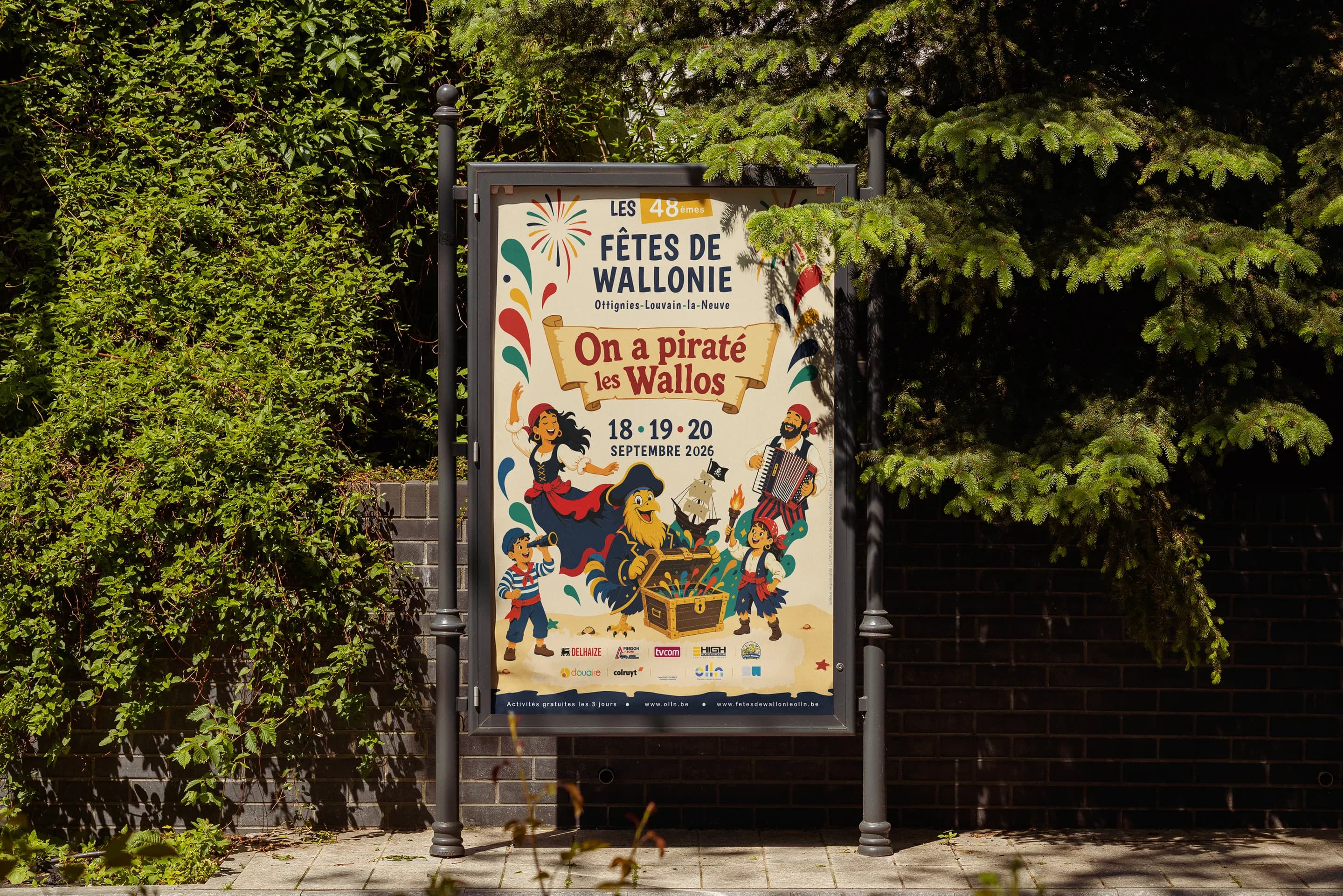 Affiche des Fêtes de Wallonie 2026 « On a piraté les Wallos » dans la rue, entourée de verdure